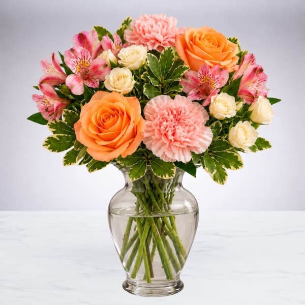Mixed bouquet of roses, carnations, and alstroemeria in a glass vase