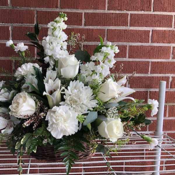 White floral arrangement in a wicker basket with roses and lilies