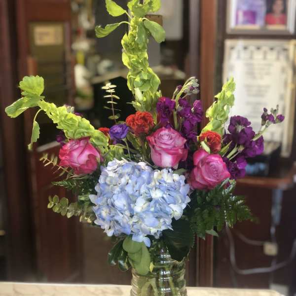 Mixed bouquet with pink roses, blue hydrangea, and purple flowers in a glass vase