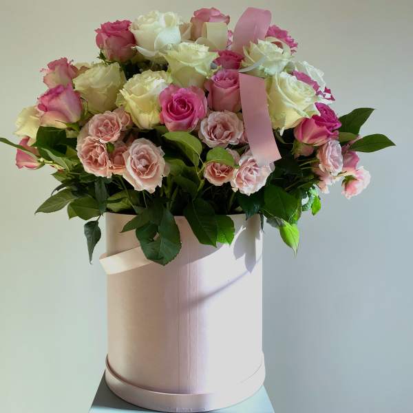 Pink and white roses arranged in a round hatbox with ribbon