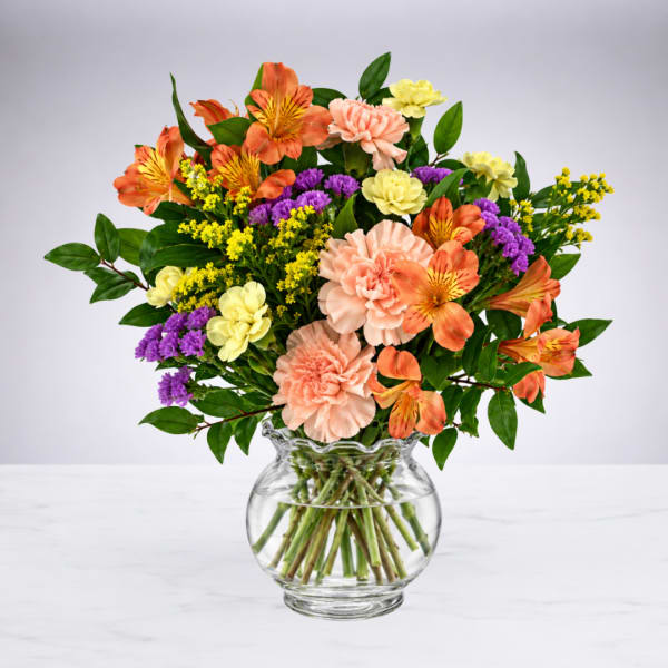 Mixed bouquet of orange, pink, yellow, and purple flowers in a glass vase