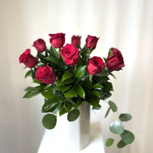Bouquet of red roses with glossy greenery in a white vase