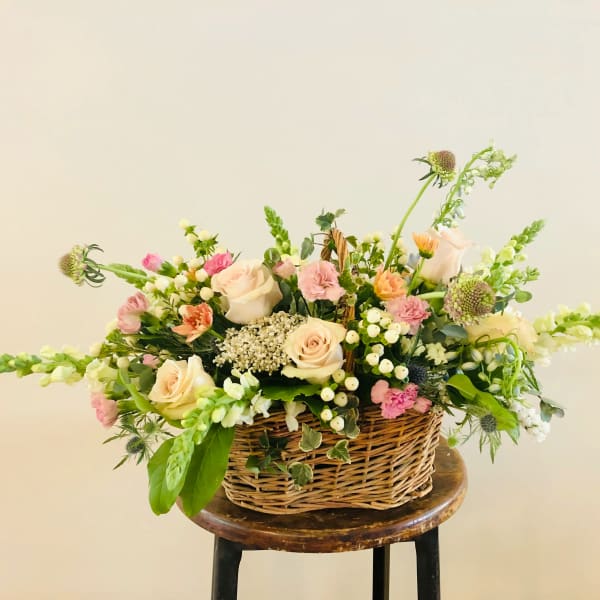 Basket arrangement of pale roses and pink flowers with greenery