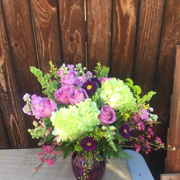 Bouquet of pink roses, green hydrangeas, and purple accent flowers in a glass vase