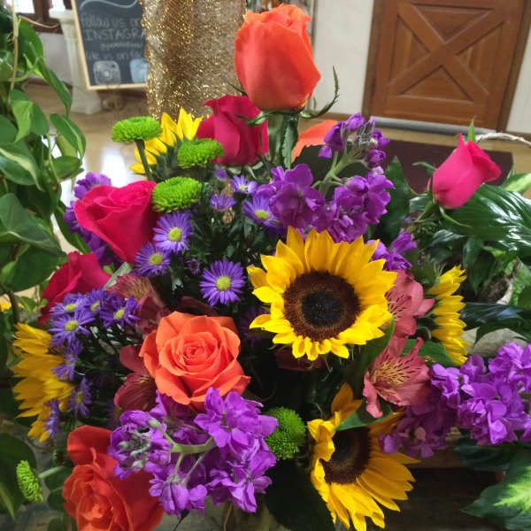 Mixed bouquet of roses, sunflowers, and purple flowers in a glass vase