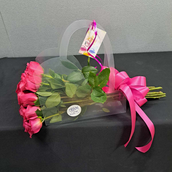 Pink roses in a clear gift bag with a bright ribbon and birthday tag