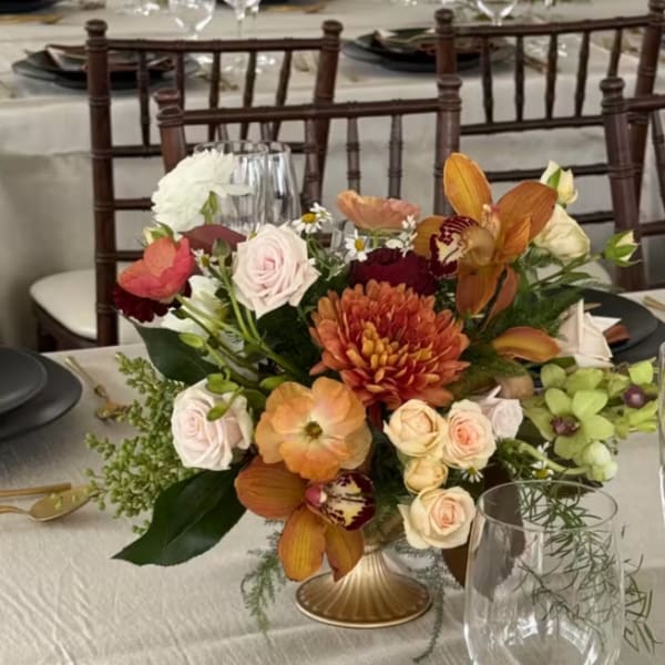 Mixed floral centerpiece in a low gold vase on a banquet table