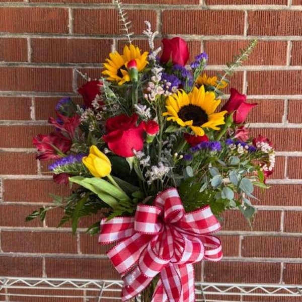 Bouquet of red roses, sunflowers, and tulips in a glass vase with a checkered bow