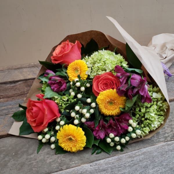 Bouquet of pink roses, yellow daisies, and green hydrangeas wrapped in paper