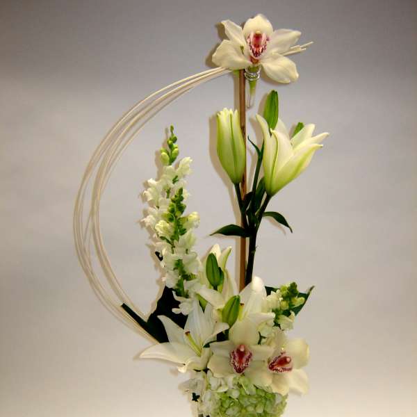 Tall white floral arrangement with lilies and orchids in a black vase
