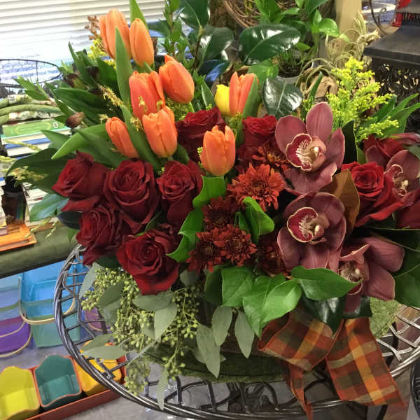 Bouquet of red roses, orange tulips, and orchids in a decorative container