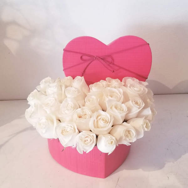 White roses arranged in a pink heart-shaped box