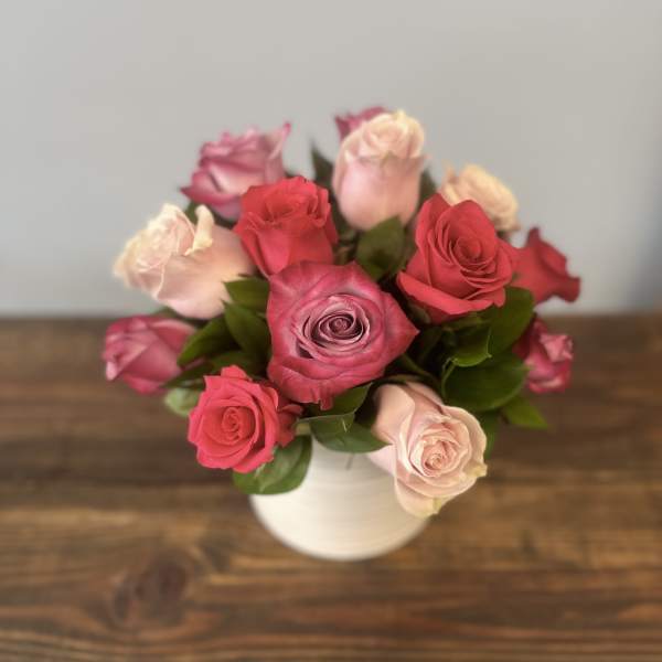 Compact arrangement of pink and lavender roses in a white vase on a wooden surface