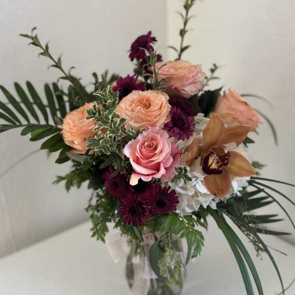 Mixed bouquet of roses, orchids, and purple blooms in a glass vase