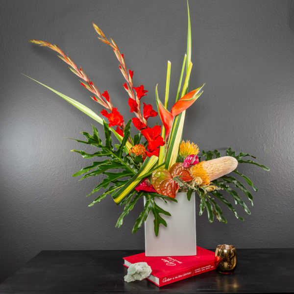 Tropical floral arrangement in a white vase with red and orange blooms