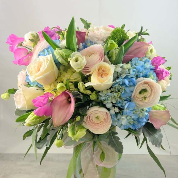 Bouquet of pastel roses, ranunculus, hydrangeas, and calla lilies in a glass vase