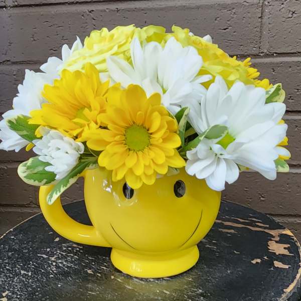 Yellow smiley-face mug filled with white and yellow daisies