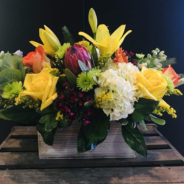Mixed bouquet with yellow lilies, roses, hydrangea, and protea in a wooden box