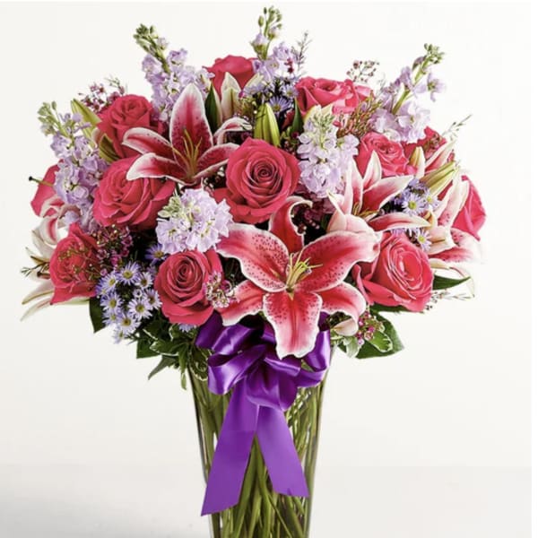 Pink roses and lilies in a clear glass vase with a purple ribbon
