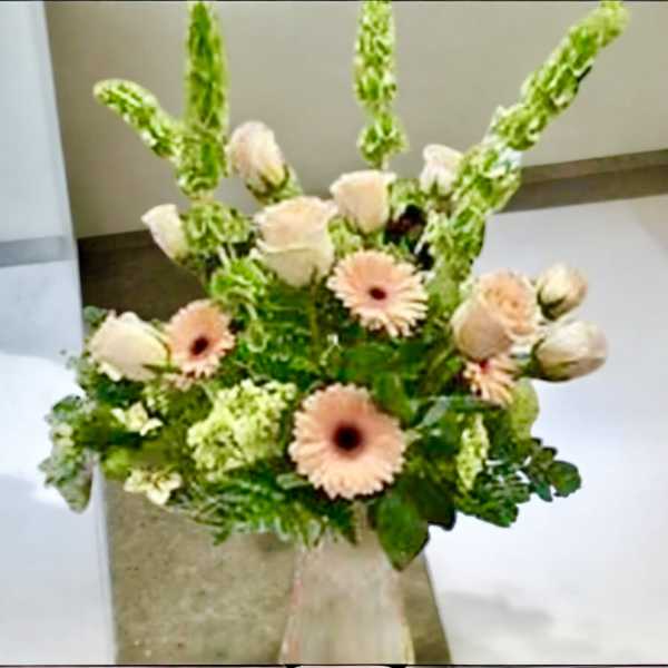 Peach gerbera daisies and pale roses in a clear vase