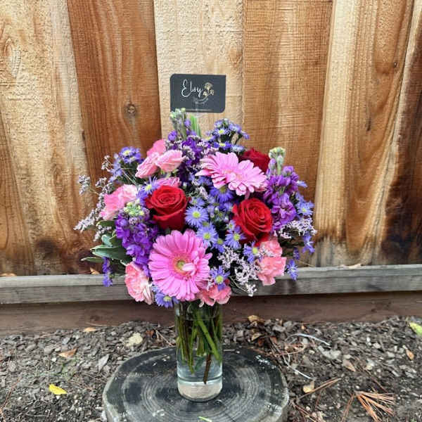 Mixed bouquet of pink, red, and purple flowers in a glass vase