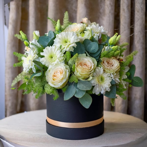 White roses and daisies in a black hat box with a gold band
