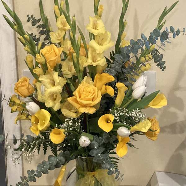 Yellow flowers and roses arranged in a clear glass vase