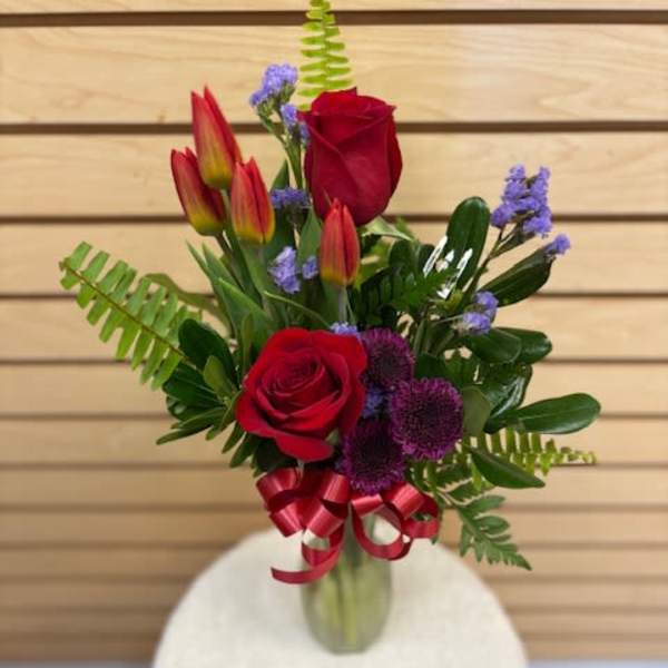 Bouquet of red roses and tulips in a glass vase with a ribbon