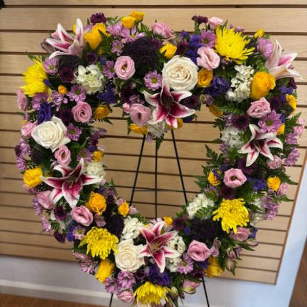 Heart-shaped floral wreath on a stand with pink, white, yellow, and purple flowers