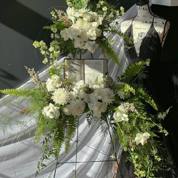 White floral standing spray on an easel beside a mannequin and draped fabric