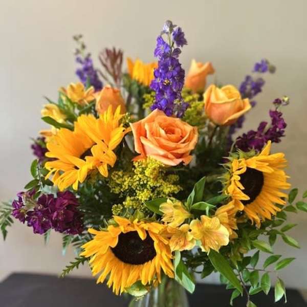 Bouquet of sunflowers, peach roses, and purple flowers in a glass vase