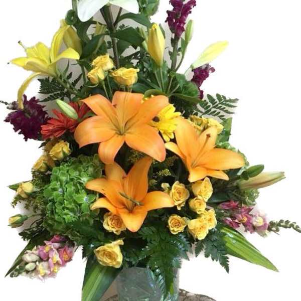 Tall mixed flower arrangement with lilies, roses, and snapdragons in a glass vase