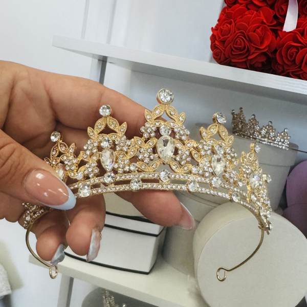 Hand holding a gold rhinestone tiara with clear crystals