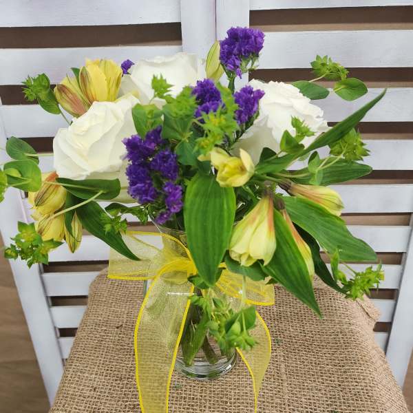 Bouquet of white roses, purple filler flowers, and yellow alstroemeria in a glass vase