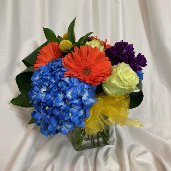Colorful bouquet with blue hydrangea, orange gerbera daisies, and a yellow ribbon in a glass vase