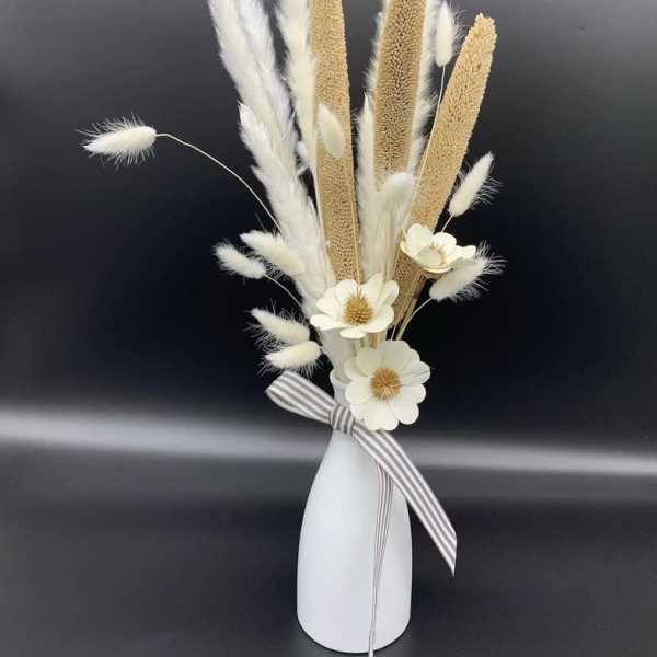 Dried grass arrangement with white flowers in a white vase