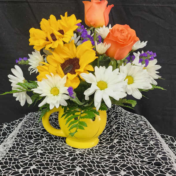 Bouquet of sunflowers, white daisies, and orange roses in a yellow mug vase