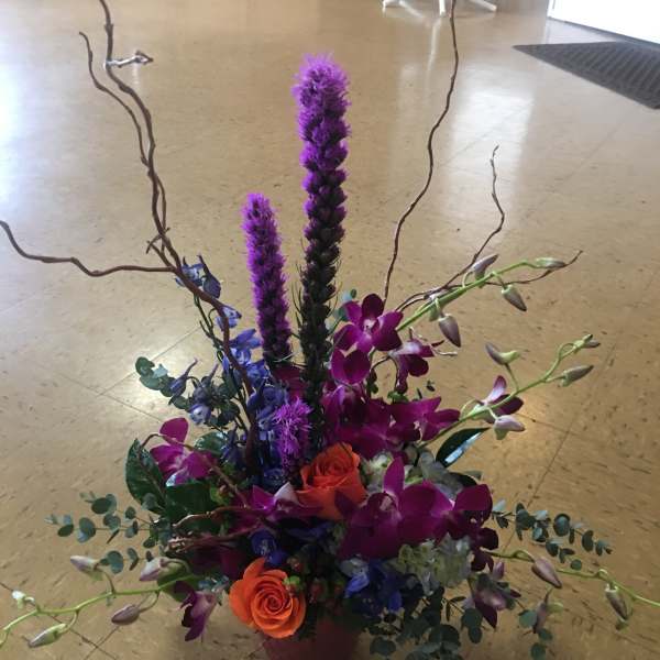 Tall floral arrangement with orange roses and purple orchids in a vase