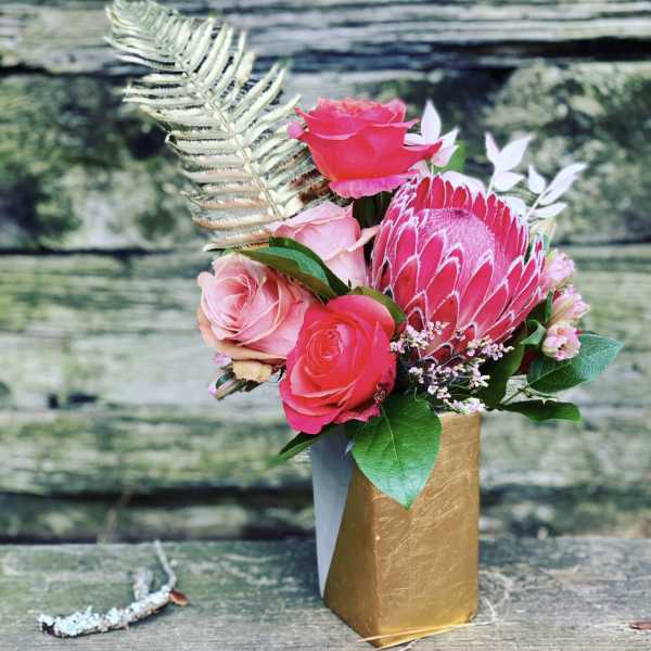 Pink roses and a protea in a gold vase