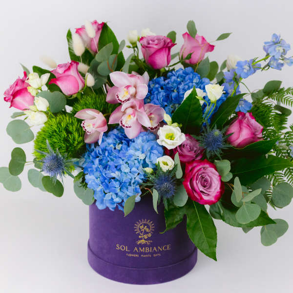 Mixed bouquet in a purple hat box with pink, blue, and white flowers