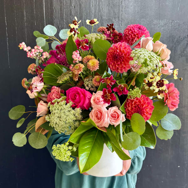 Mixed pink and coral bouquet in a white vase held in front of a dark wall.