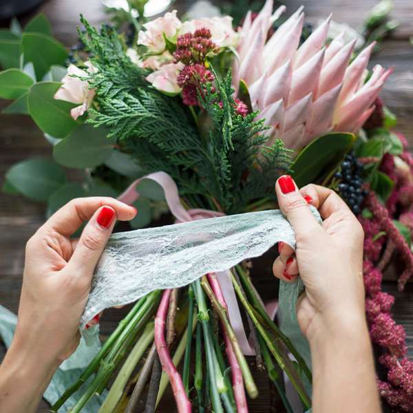 Hands tying lace around a pink and green bouquet