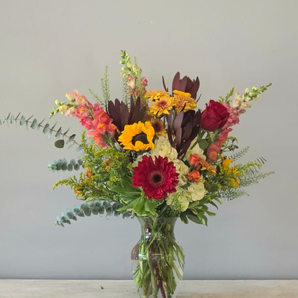 Mixed bouquet of sunflowers, gerbera daisies, roses, and snapdragons in a glass vase
