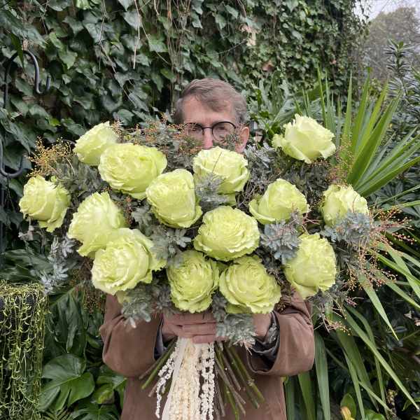 Person holding a large bouquet of pale green roses