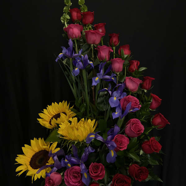 Tall arrangement of red and pink roses with purple irises and yellow sunflowers