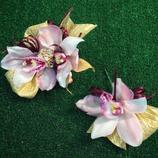 Two orchid corsages with gold ribbon accents on green turf