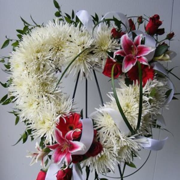 White floral wreath with red roses and pink lilies on a stand