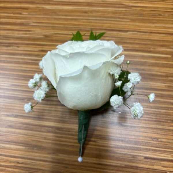 White rose boutonniere with baby's breath on a wooden surface