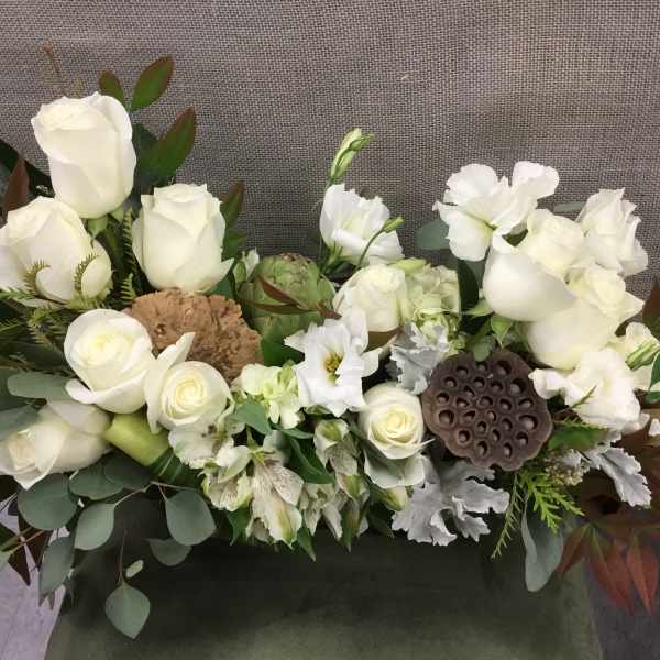 White roses and white blooms arranged with greenery in a low centerpiece