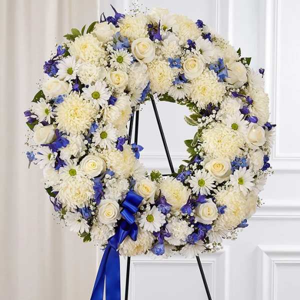 White floral wreath with blue accents on a stand and ribbon